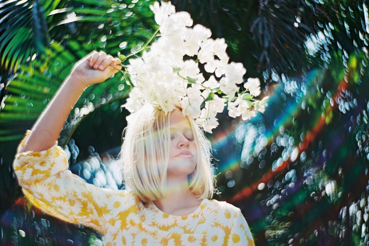 An image of someone in floral dress and holding a bushel of flowers being enhanced with a rainbow lens flare