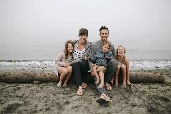 A picture of a family sitting on a log at the beach.