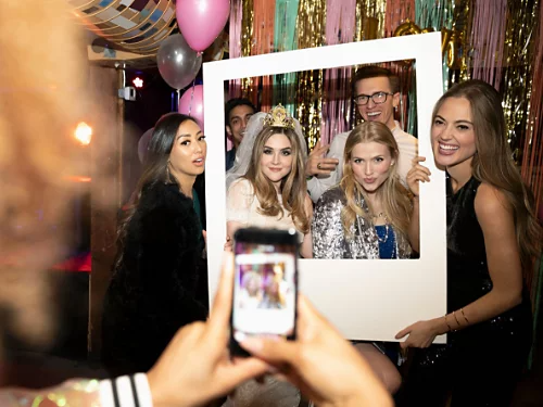 A picture of people taking a photo at a party against a celebratory backdrop with props.