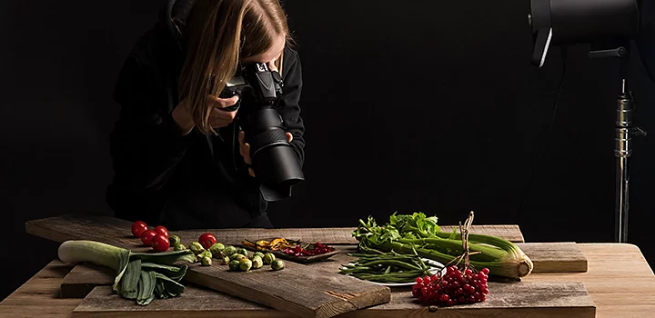 A food photographer creating stock photography of a rustic vegetable tablescape in a dark room