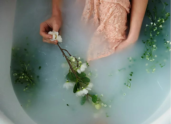 A photo of a person sitting in a milk bath with flowers used as props.