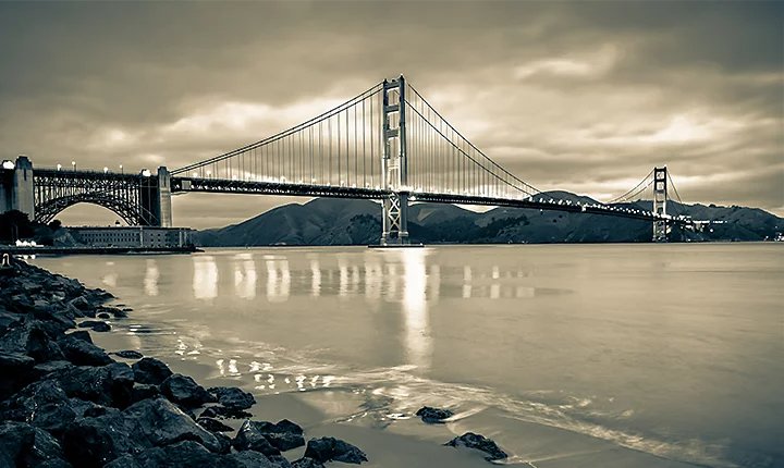 A sepia photo of a bridge over smooth water at night