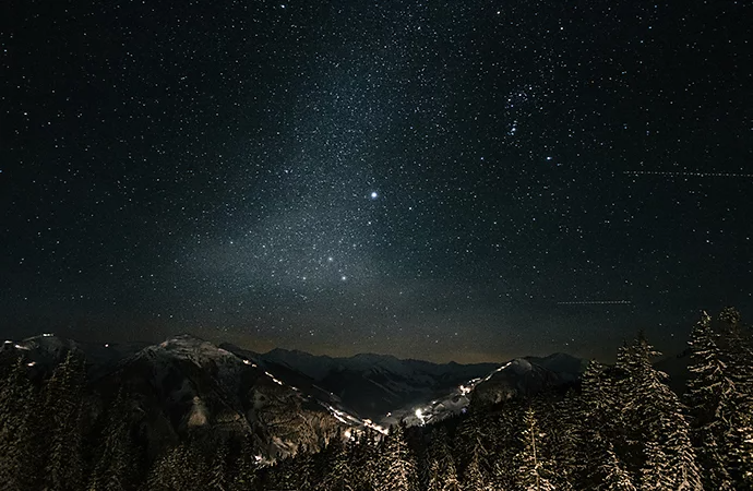 Photo of stars in the sky over a mountain and forest landscape