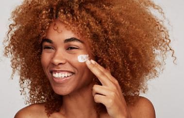 A model flashing a bright smile while applying facial cream as they look past the camera