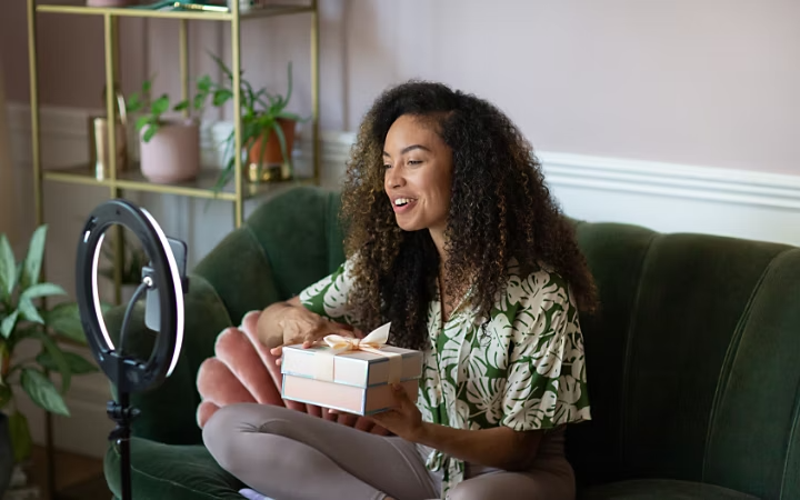 A photo of a person recording a selfie video on the couch in their living room.