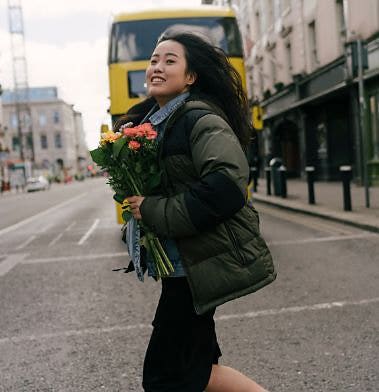 Someone carrying flowers crossing the street in London behind a yellow double-decker bus