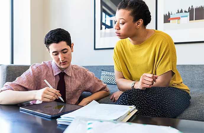 Photo of two people reviewing notes on a tablet device while sitting in a living room