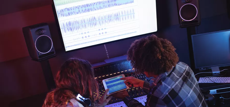 Two people at a studio computer with an audio file on screen being compressed