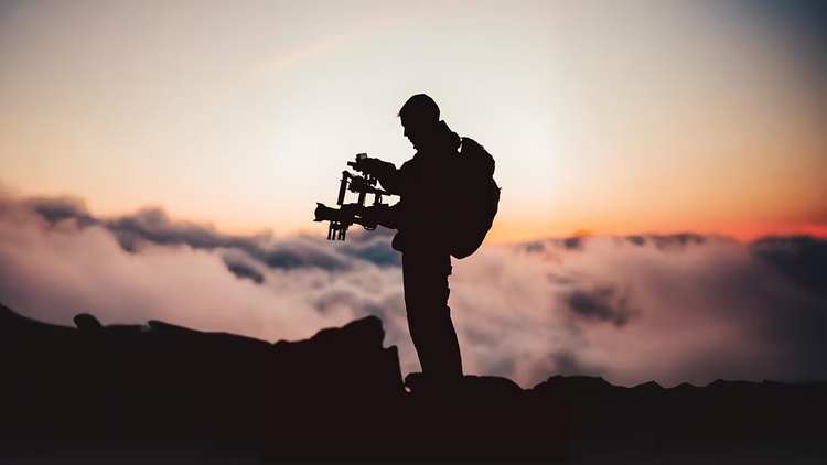 Person holding camera on the cliff during the sunset