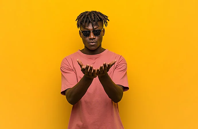 Man holding his palms out facing upward stands in front of a vibrant yellow wall in an example of low-key lighting