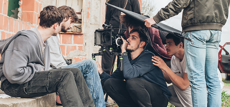 A production crew filming a-roll of two actors sitting outside on a window sill