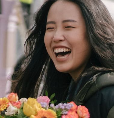 A person holding flowers and laughing in a narrow close-up shot