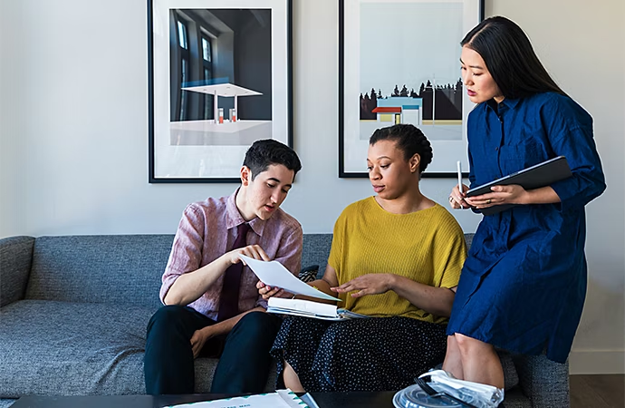 Photo of three people reviewing notes for a training video on a couch in a living room