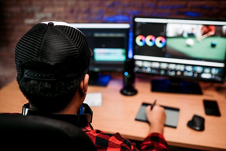 Man at desk drawing on design pad in front of two computer monitors.