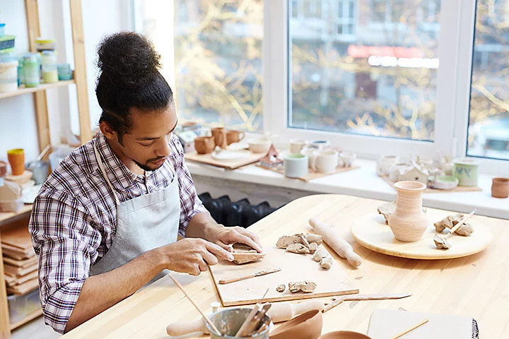 Man with apron cutting clay at workbench.