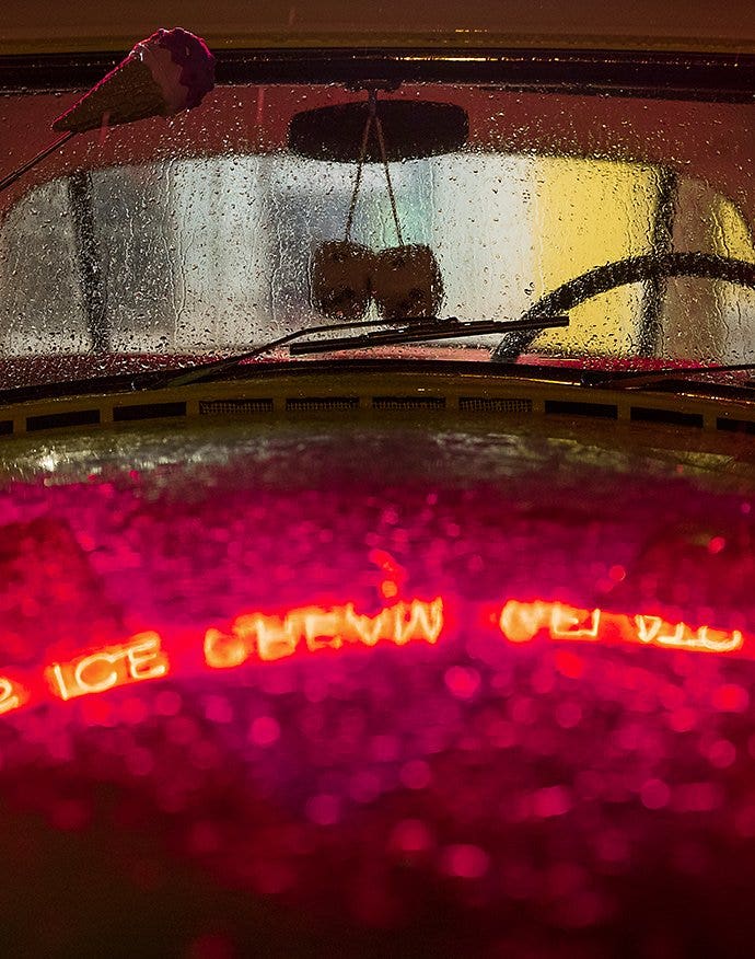 A reflection of a neon light sign on the hood of a car that was recently rained on