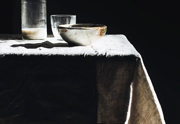 A table with two glasses and a bowl on it in front of a black background