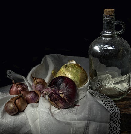 Still-life photo of onions on a mussed tablecloth by an empty whiskey bottle