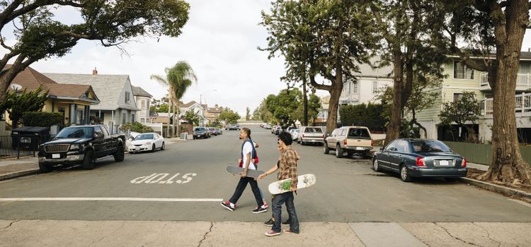 Young skateboarders walk across a suburban street