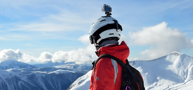 Eine Person, die am Gipfel eines verschneiten Berges steht und einen Helm mit daran befestigter Kamera trägt; das Footage soll nach der Abfahrt stabilisiert werden.