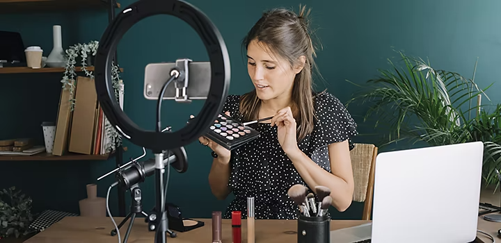 Eine Person, die mit Smartphone, Stativ und Beleuchtung ein Make-up-Tutorial mit sich selbst aufnimmt.