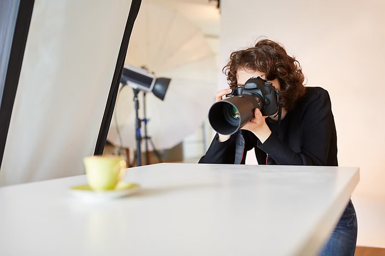 Eine Frau hält eine Digitalkamera in der Hand, um ein Produktvideo aufzunehmen. Sie filmt eine gelbe Tasse.