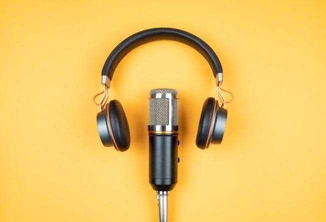 A podcast microphone and a pair of headphones against a yellow background