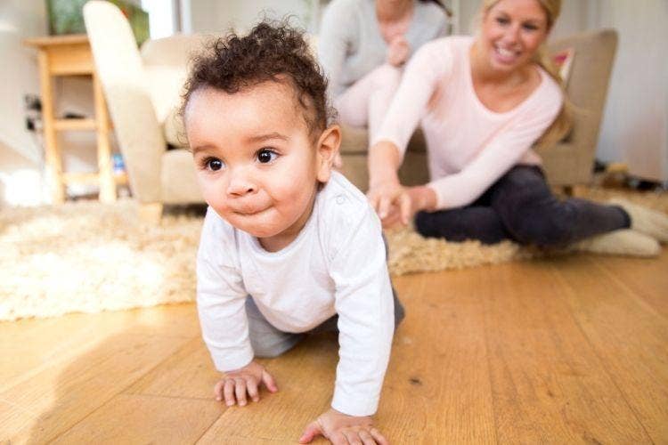 A baby crawling on the floor with a person and a couch Description automatically generated