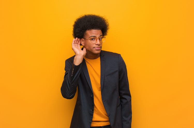 Man listening A man in a yellow shirt and black blazer cups a hand to his ear in a 'listening' pose.