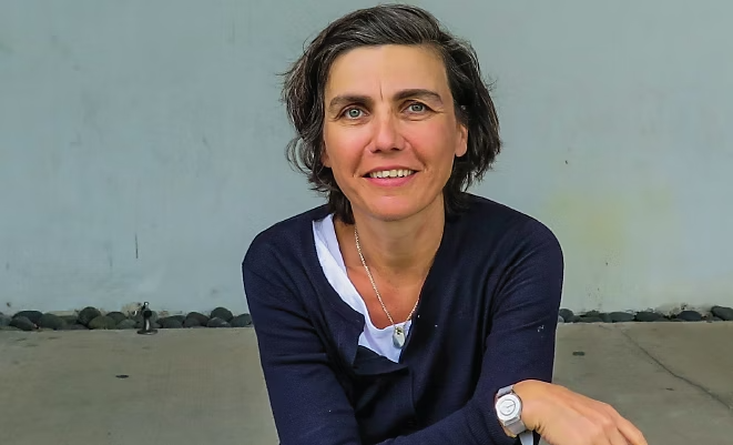 A closeup of Nathalie Sauvaire smiling in front of a blue building.