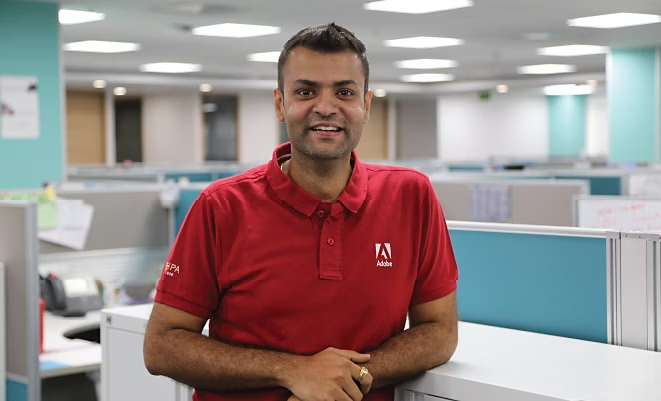 Manu Malhotra smiling in an office space while wearing a red Adobe shirt.