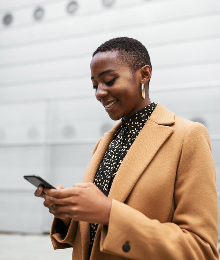 A person standing and smiling while using their mobile phone