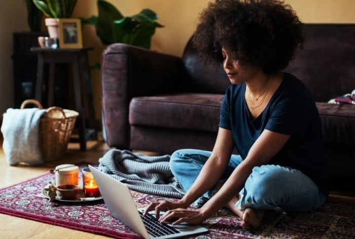 A person editing a PDF on their Mac while sitting on a Persian rug with coffee and candles next to them