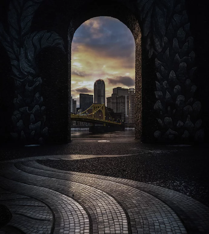 Photo of a bridge connecting to a city seen through a door arch