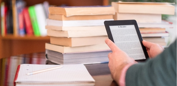 La foto muestra un lector de libros electrónicos frente a una pila de libros.