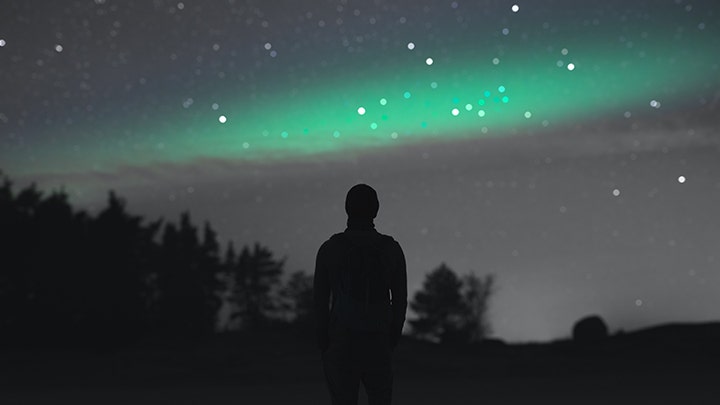 Imagen de la silueta de una persona mirando al cielo en una noche llena de estrellas.