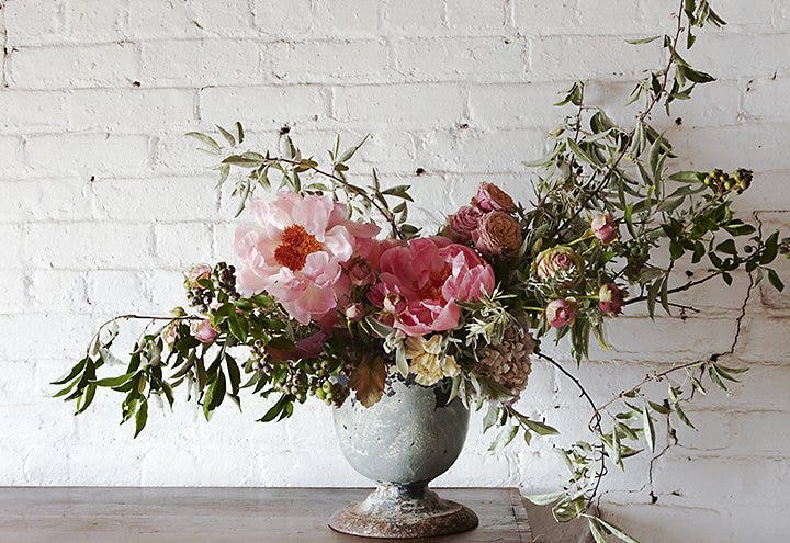 Arreglo de flores en un vaso gris delante de una pared blanco de estilo industrial