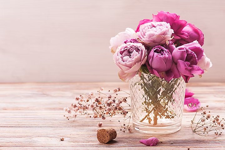 Vaso lleno de rosas en una mesa de madera con un torcho y otras flores