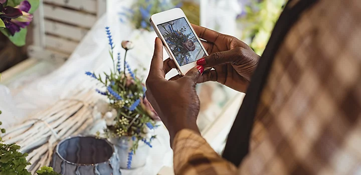 Persona con uñas pintadas sacando una foto con su móvil de un adorno floral