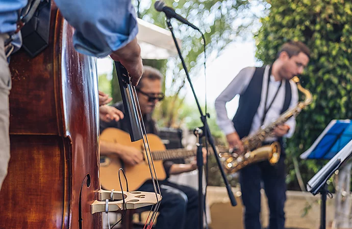 A close-up photo of a stand-up bass being played and two out-of-focus band members playing in the background