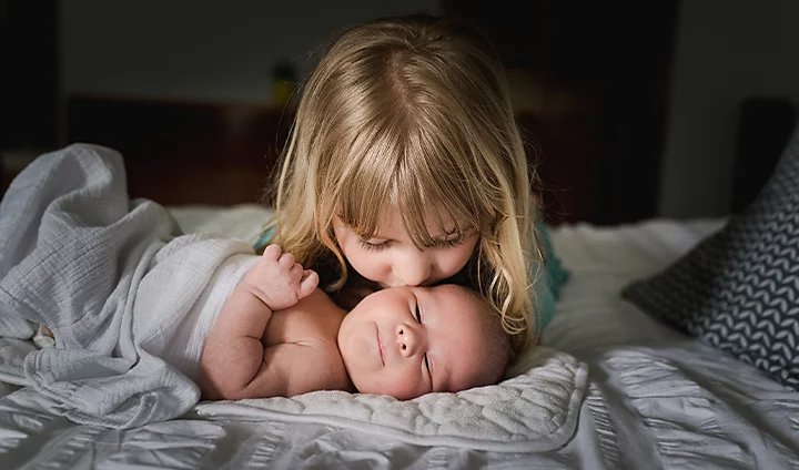 A child kissing their newborn sibling