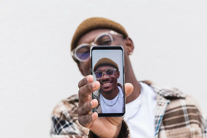 A photo of a person holding up their smartphone to the camera and showing a selfie photo of themself on the screen.