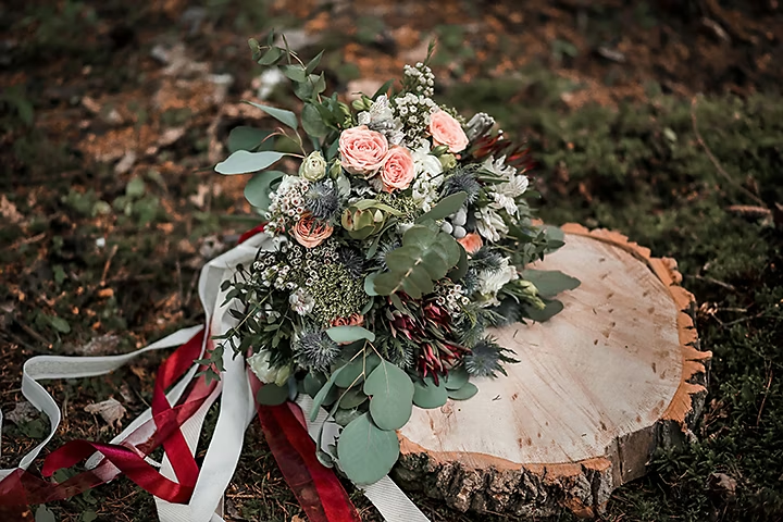 Arreglo de flores con cintas sobre un tocón de árbol colocado en hierba