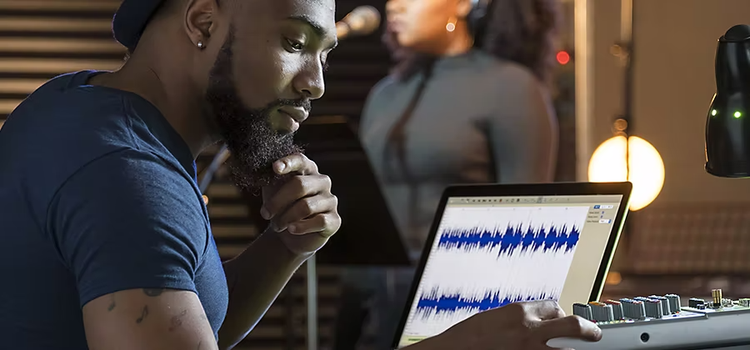 Hombre usando un mezclador de audio junto a su ordenador portátil para ecualizar el sonido