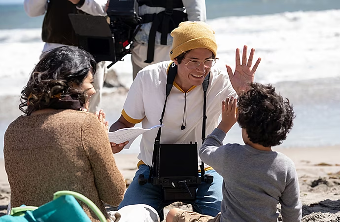 Un director chocándole los cinco a un niño actor en un escenario de producción de vídeo montado en la playa