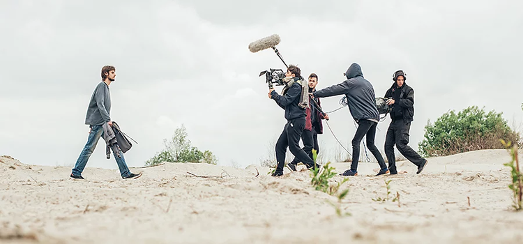 Un equipo de producción de vídeo rodando una escena de un cortometraje en el exterior con un actor caminando por un desierto