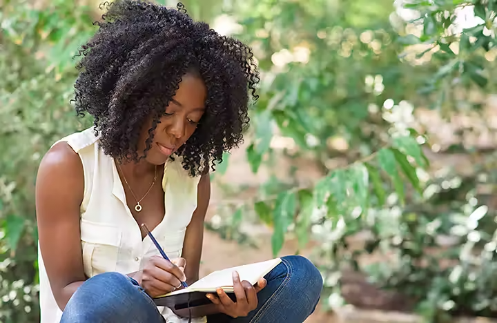 Una persona sentada y escribiendo en una libreta