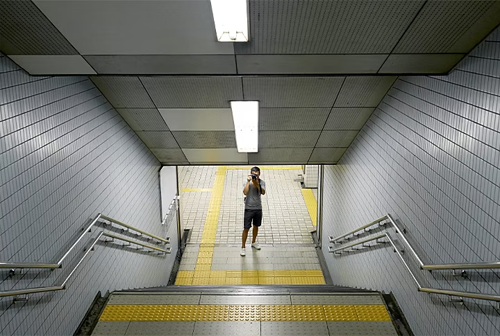 Foto tomada desde lo alto de unas escaleras de una boca de metro con luces de tungsteno en el techo