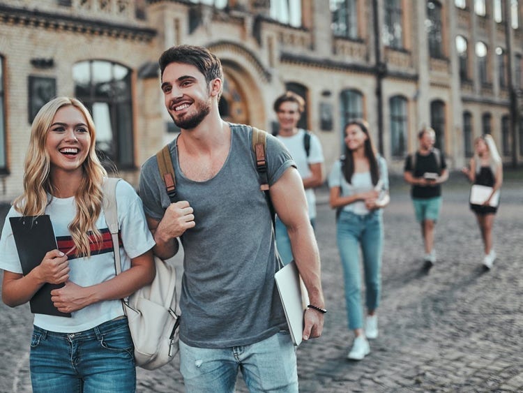 A group of young adults students conversing and walking, with a historical building in the background