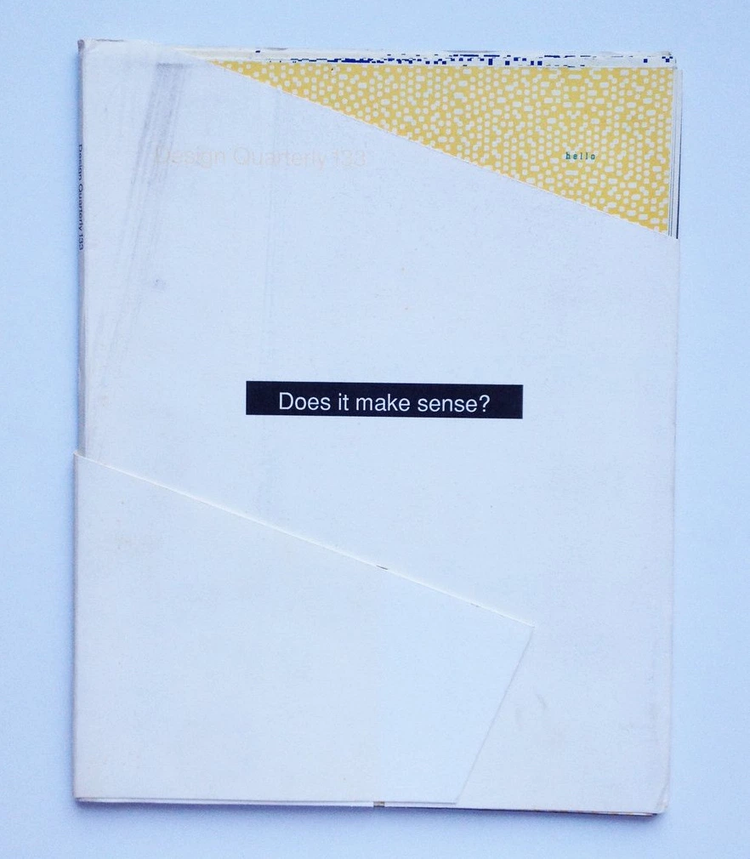 A picture containing a primarily white folded poster with a black bar at center with the white text "Does it make sense?" A corner of yellow patterned paper with the small blue text "hello" peeks out at top right and a faint orange text next to it reads "Design Quarterly 133."